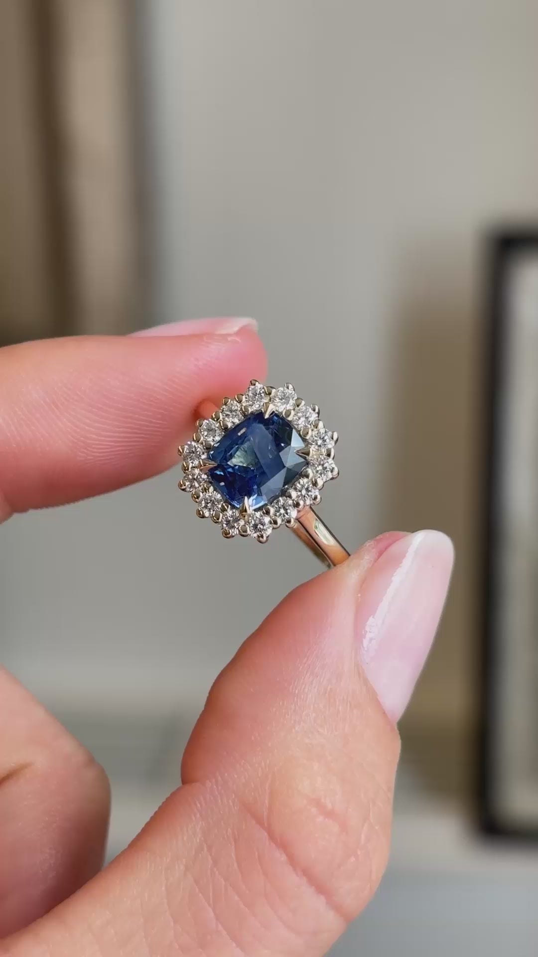 A video showing a vintage-inspired, blue sapphire with a diamond halo set in yellow gold held between fingers.