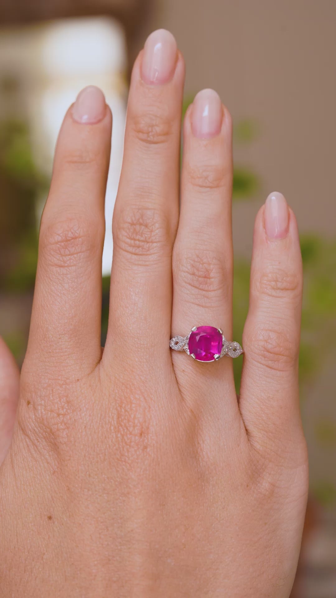 A video of an Antique, 1920s Art Deco pink ruby flanked solitaire engagement ring in white gold worn on a wedding finger and rotated to showcase the profiles and fit of the ring when worn. 