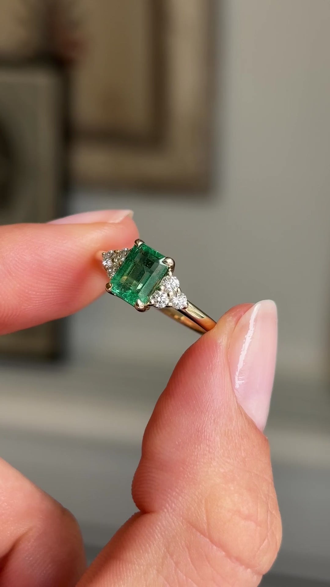 Video of an Antique-inspired, Emerald and diamond cluster trefoil engagement ring in yellow gold, held between two fingers rotated to see the side profile of the ring