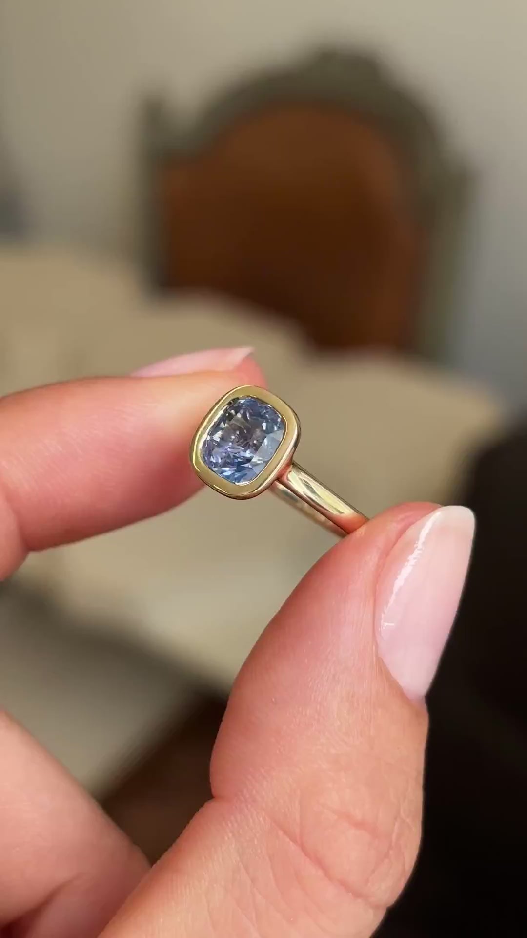 Video of an Antique-inspired gold solitaire engagement ring held between two fingers and rotated slowly to showcase the light purple cushion-cut sapphire. 