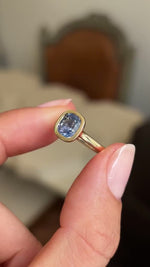 Video of an Antique-inspired gold solitaire engagement ring held between two fingers and rotated slowly to showcase the light purple cushion-cut sapphire. 