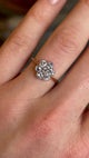 A hand moving around slowly wearing an Edwardian daisy diamond cluster ring with an 18ct yellow gold band with a blurred background