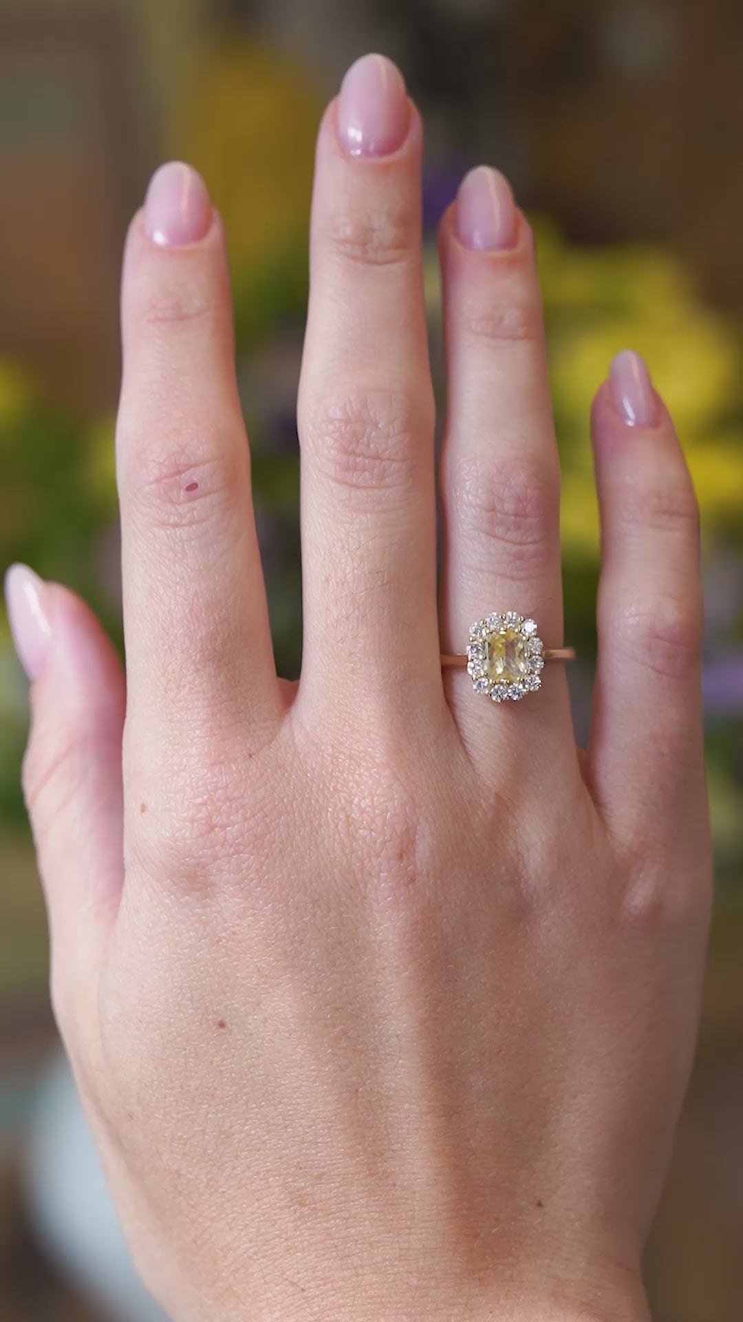 Pale yellow sapphire and diamond cluster engagement ring worn on hand with a gentle motion.