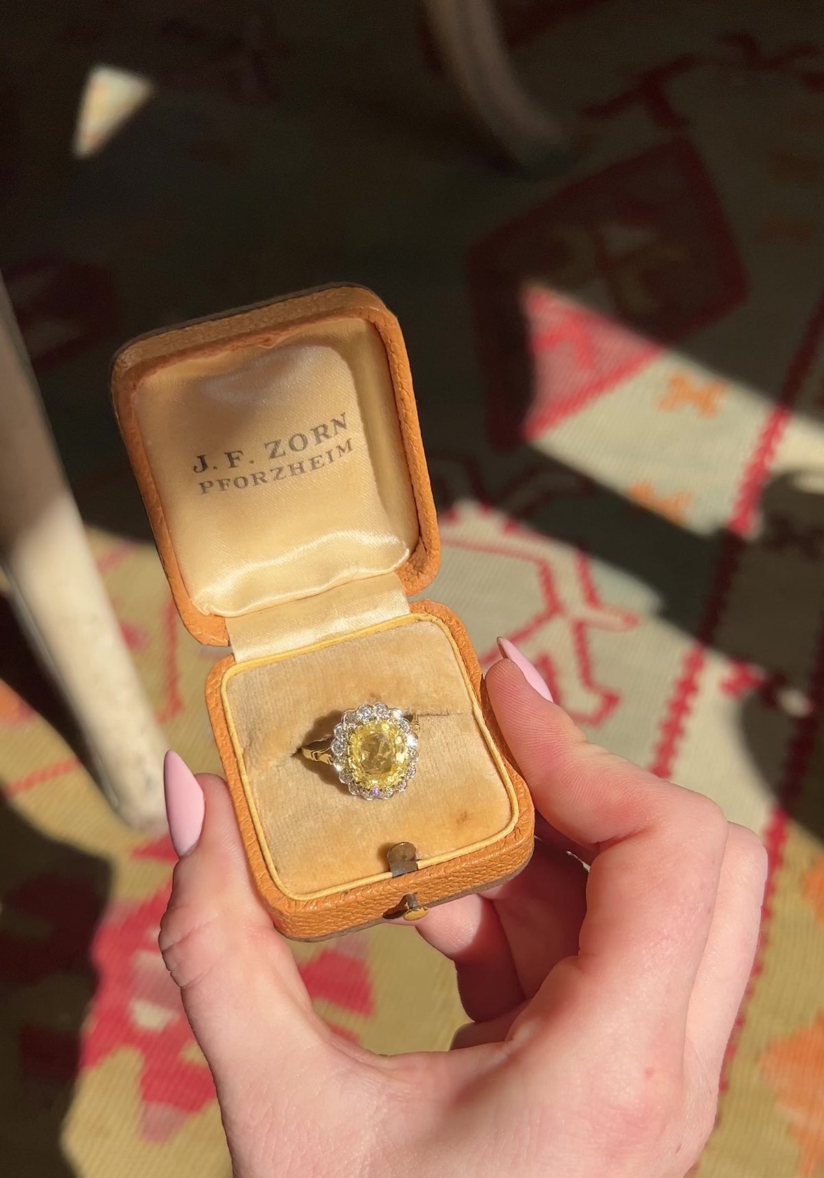 A video of a vintage yellow sapphire cluster ring in yellow gold in an open vintage box held in a hand a rotated to show it sparkle in the light.