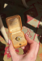 A video of a vintage yellow sapphire cluster ring in yellow gold in an open vintage box held in a hand a rotated to show it sparkle in the light.