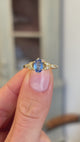 Blue sapphire and diamond engagement ring showcasing an oval blue sapphire centre stone with diamond-set trefoil shoulders in the form of laurel leaves, held by hand to highlight the setting and craftsmanship.