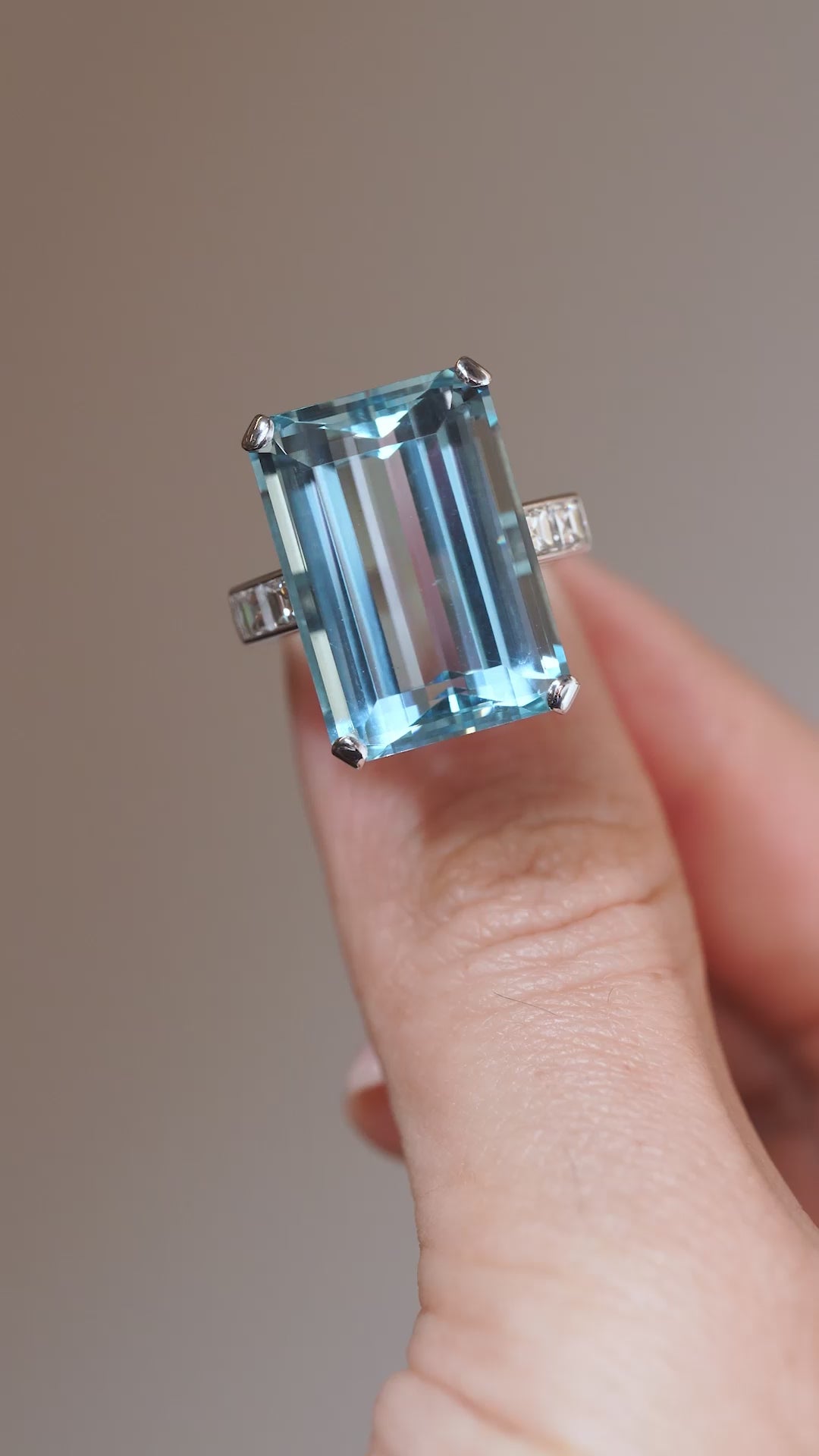 A close-up video of a vintage 1970s aquamarine and diamond cocktail ring held between fingers, showcasing its large rectangular gemstone and geometric white gold design.