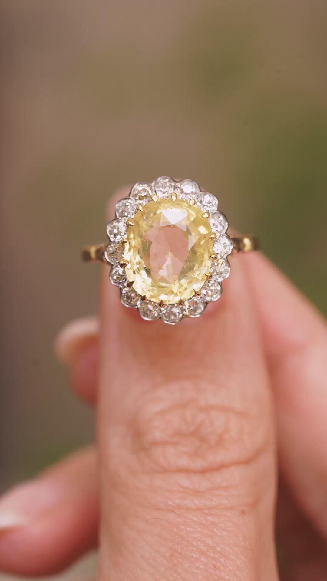 a video of Vintage, 1950s yellow sapphire and diamond cluster engagement ring held in between the fingers and turned to show off angles