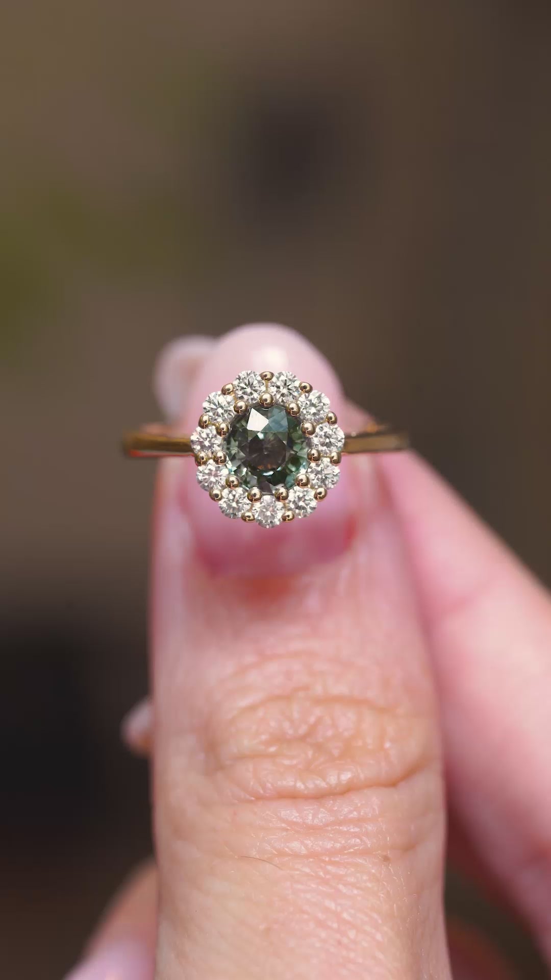 A close-up video of an antique-inspired yellow gold ring featuring an earthy green sapphire surrounded by a diamond cluster.