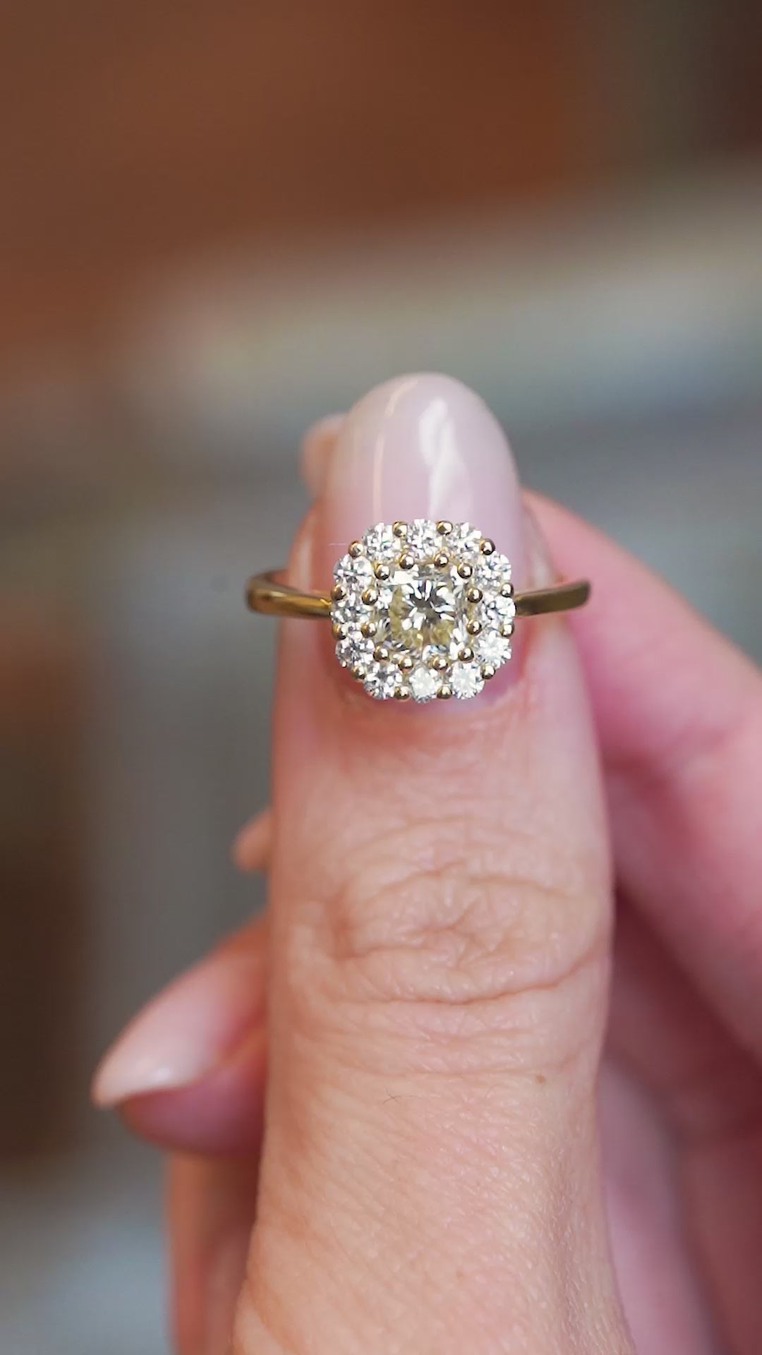Diamond cluster engagement ring worn on finger showing ring details with subtle movement.
