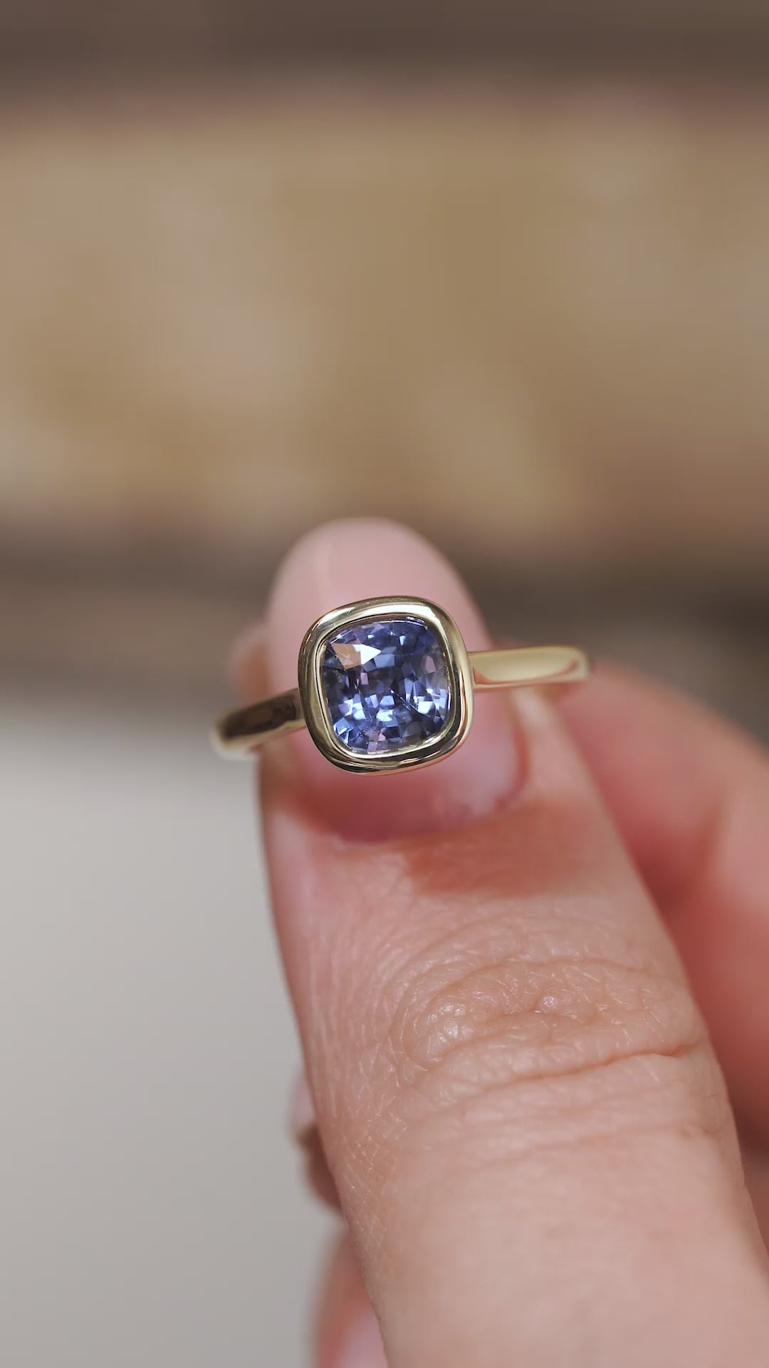 A close-up video of the sapphire engagement ring held between fingers, showcasing the gemstone's facets and polished gold surround.