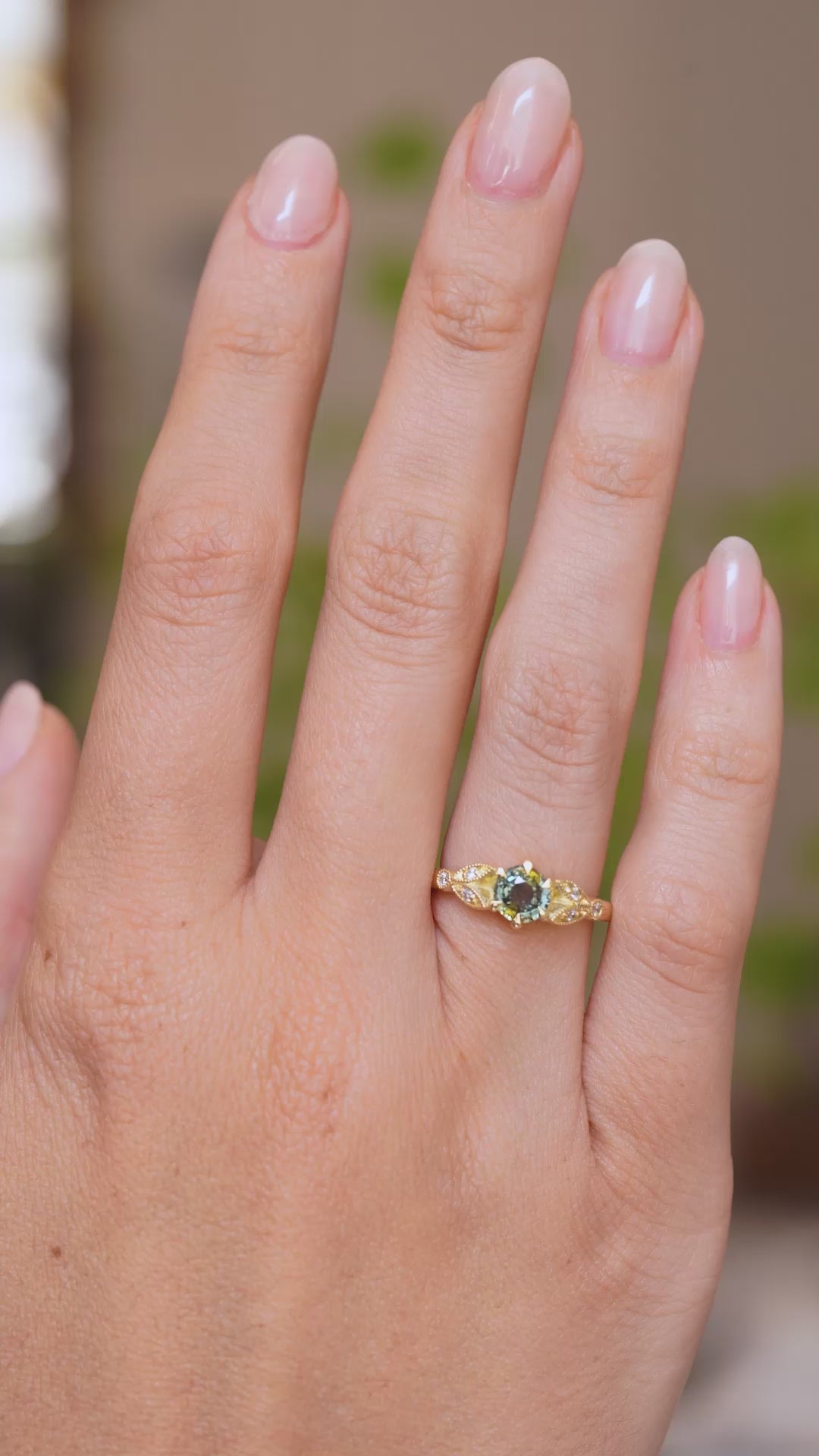  A video of a hand wearing a Vintage-inspired, Green sapphire and diamond engagement ring in yellow gold on a wedding finger. 