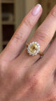 An antique-inspired, vibrant yellow sapphire and diamond cluster engagement ring in yellow gold worn on a hand rotated to show the ring.