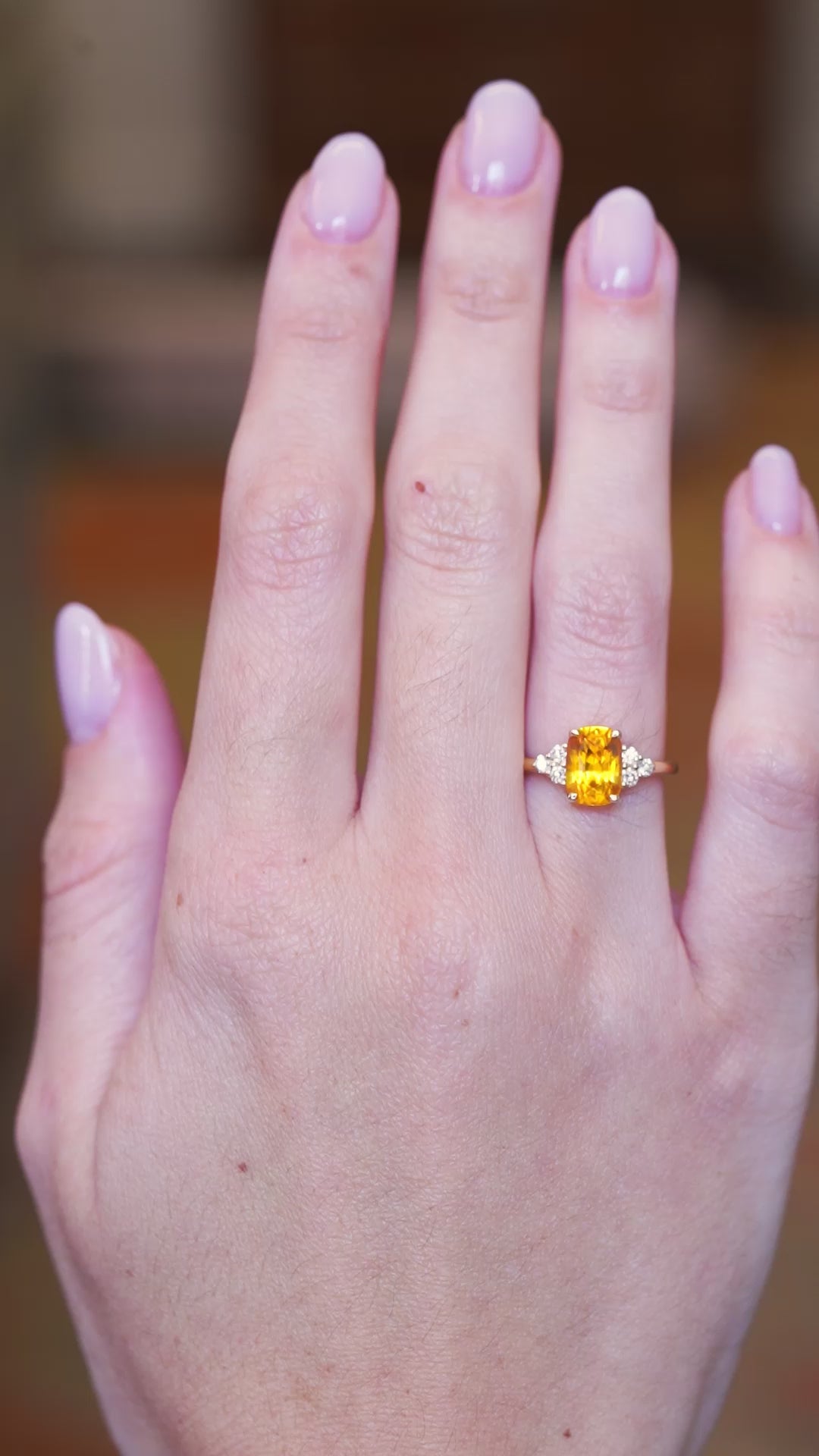 Orange cushion cut sapphire and diamond cluster trefoil ring worn on hand showing fit and natural movement.