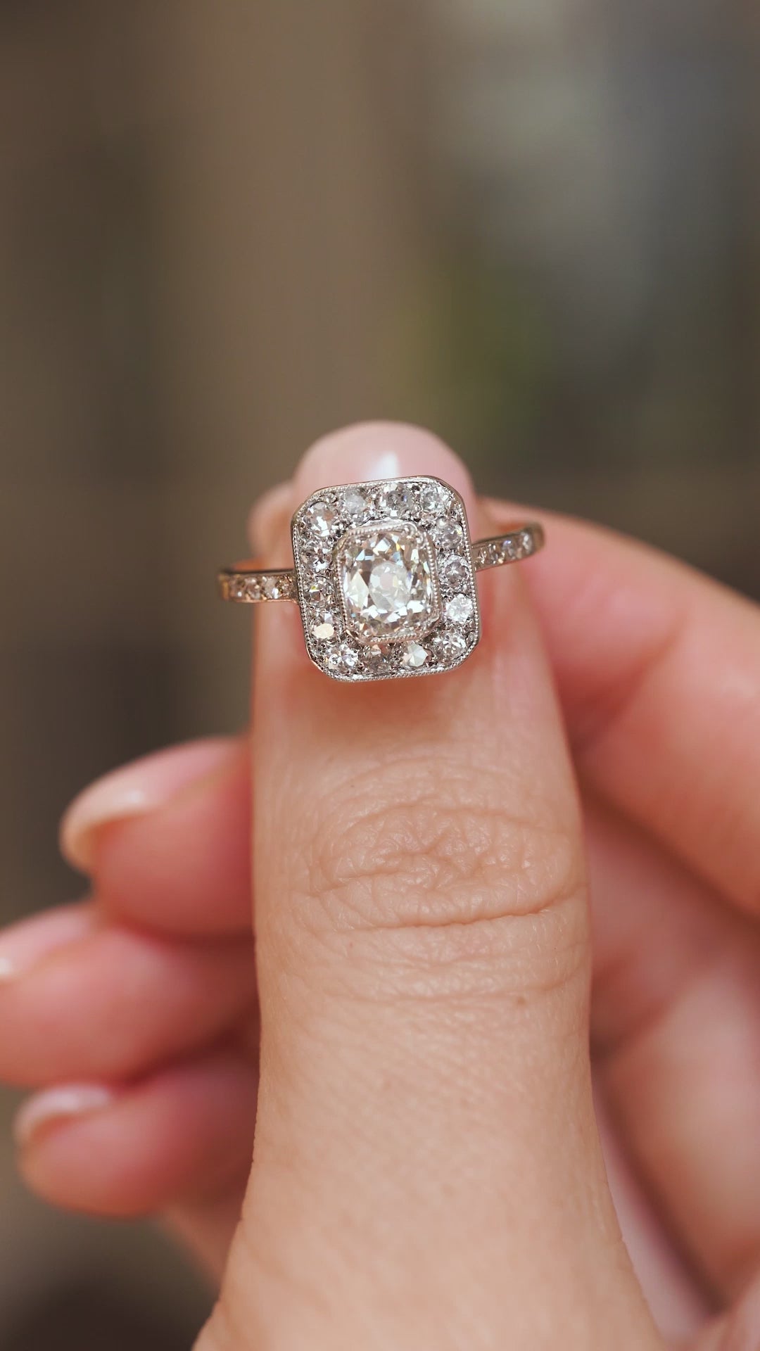 Video close-up of an antique Edwardian diamond ring balanced on a fingertip, displaying its intricate platinum cluster setting.