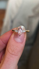 Pink Marquise-cut sapphire and diamond three-stone engagement ring held and rotated to show details of setting. 