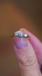 Three stone diamond ring worn on hand with subtle movement and natural light reflections.