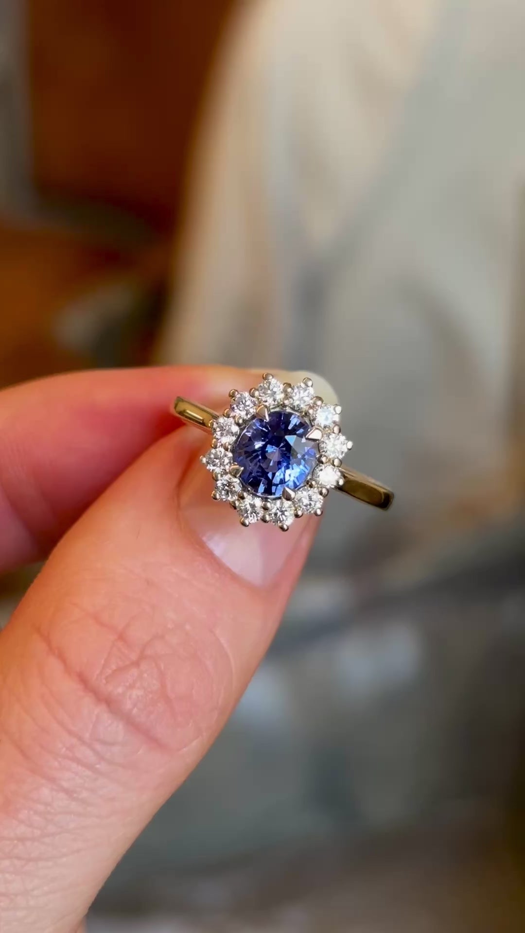 Blue sapphire and diamond cluster engagement ring held in fingers on video to show details and sapphire colour. 