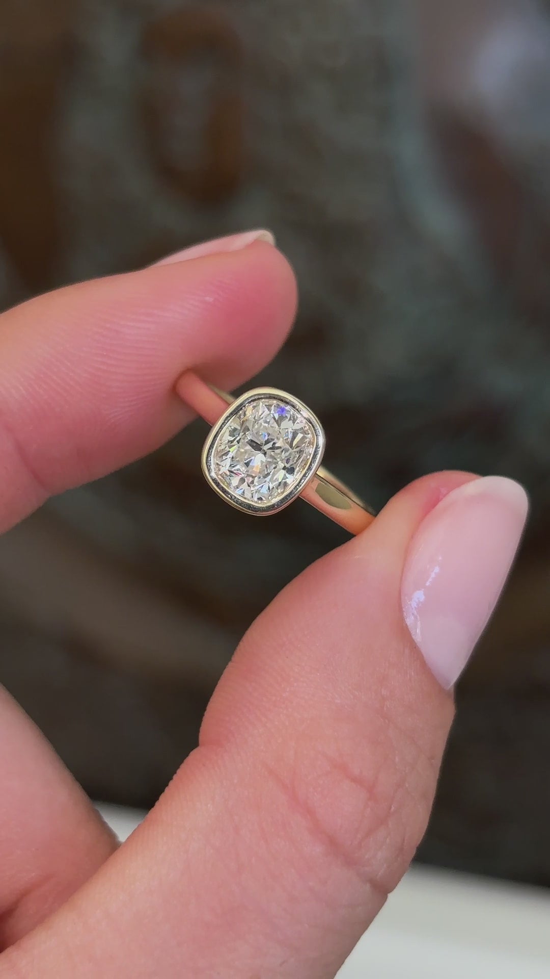 Antique-inspired cushion old-cut diamond solitaire engagement ring featuring a cushion old-cut diamond in a timeless solitaire design, displayed while held by hand.