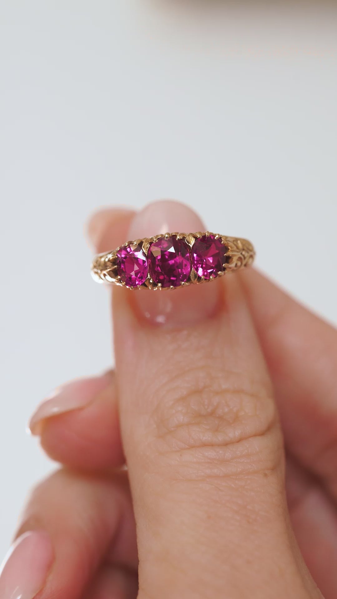 Video close-up of the antique Cambodian ruby ring balanced on a fingertip, highlighting the cushion-cut stones and gold detailing.
