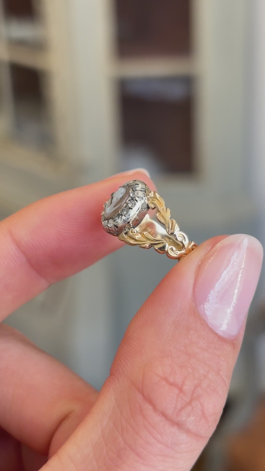 Antique Georgian forget-me-not cameo cluster ring featuring a carved forget-me-not cameo within a decorative cluster setting, held by hand for detailed viewing.