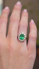 A video of a vintage 1950s oval-cut emerald and diamond cluster engagement ring in white gold worn on a hand.