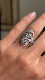 Antique Art Deco diamond cluster cocktail ring in platinum worn on hand, showcasing intricate filigree detailing and sparkling old-cut diamonds, filmed against a softly lit vintage interior backdrop.