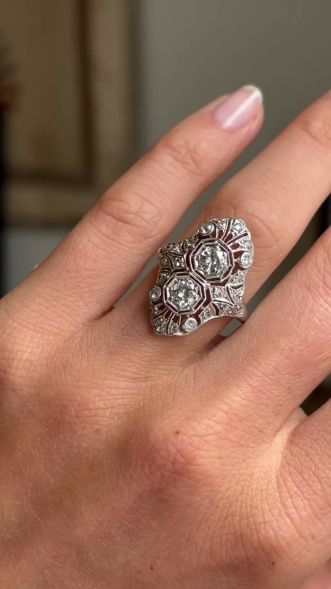 Antique Art Deco diamond cluster cocktail ring in platinum worn on hand, showcasing intricate filigree detailing and sparkling old-cut diamonds, filmed against a softly lit vintage interior backdrop.