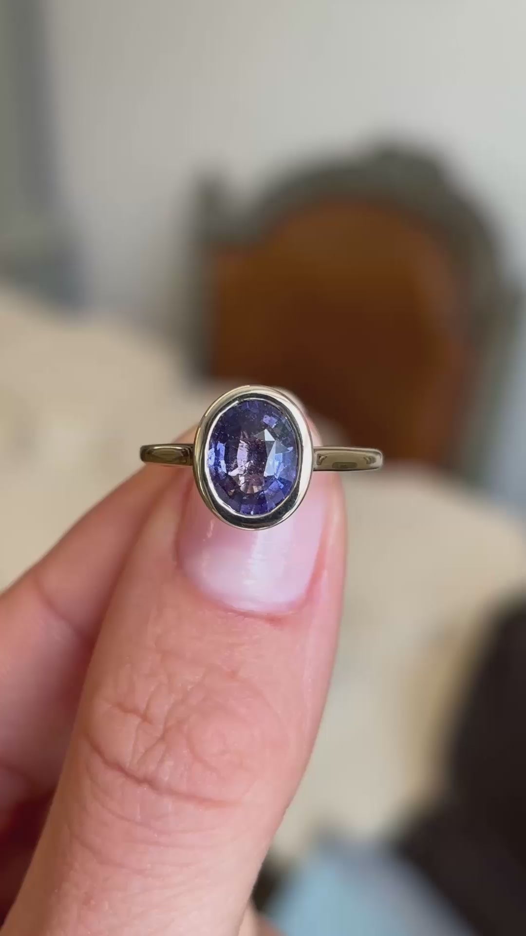 An Antique-inspired, royal purple oval sapphire solitaire ring set with a rub-over setting in yellow gold.