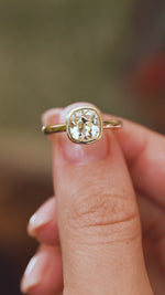 Video close-up of an old-mine cut diamond ring balanced on a fingertip, displaying the cushion stone and polished gold surround.
