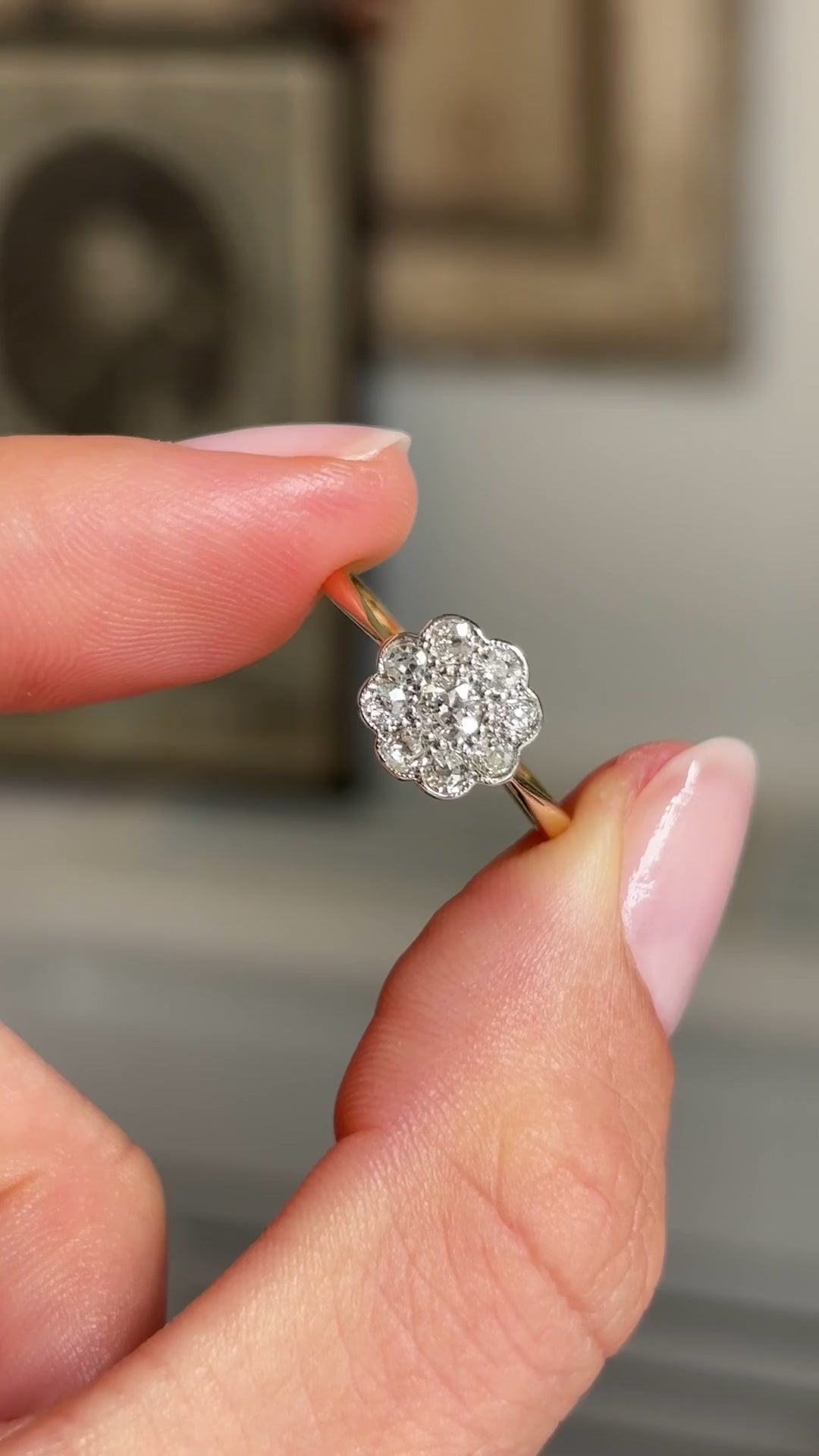 Close up video of an Antique, Edwardian old-cut diamond cluster ring in gold, held between two fingers and rotated slowly to view all angles of the ring.