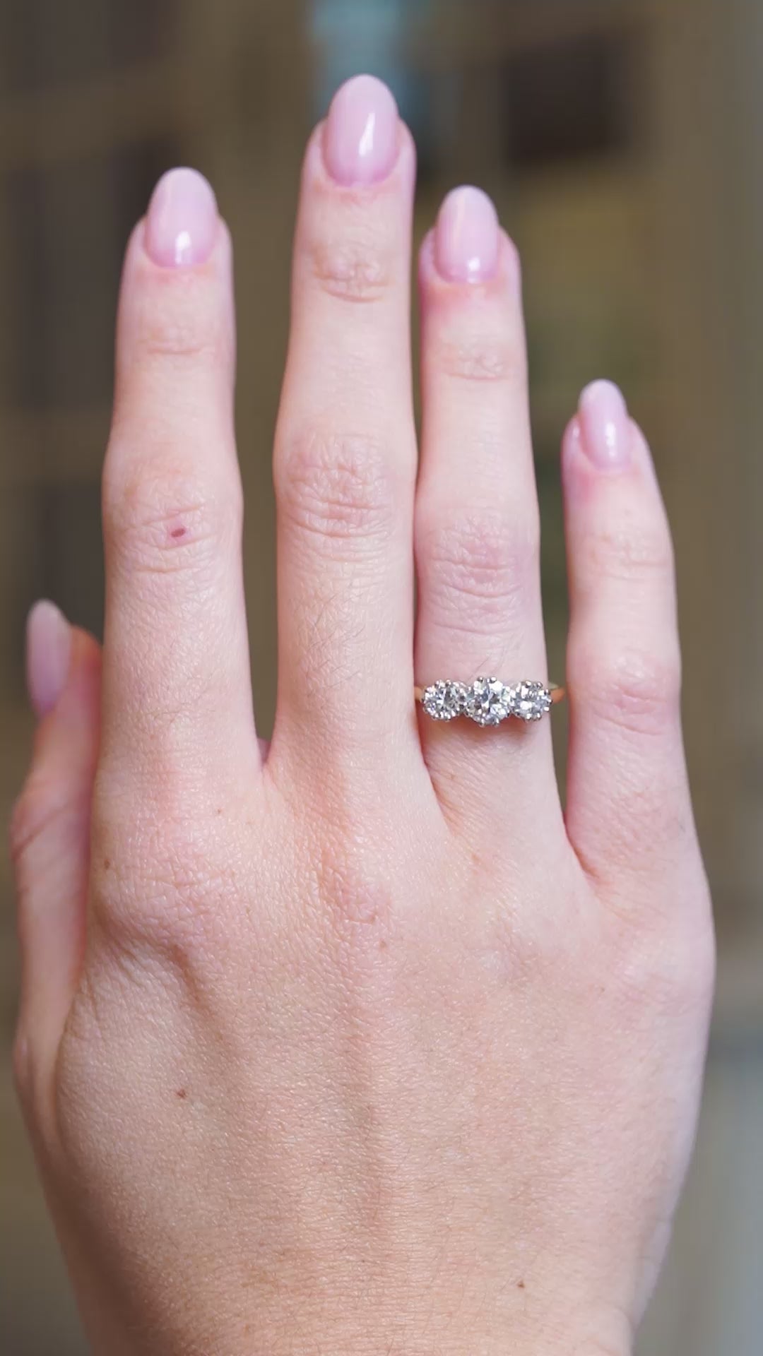 Antique Art Deco diamond three-stone ring worn on hand with sparkling graduated diamonds and yellow gold band.