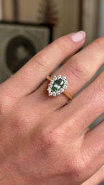 Antique-inspired pear-cut green sapphire and diamond cluster ring in yellow gold worn on hand, showcasing the vibrant green sapphire, sparkling diamond halo and elegant craftsmanship against a softly lit vintage interior backdrop.