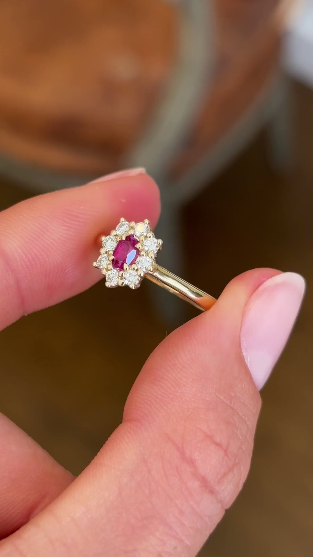 Close-up video of an antique-inspired yellow gold cluster ring showcasing an oval-cut ruby framed by sparkling diamonds, highlighting rich colour, brilliance and fine craftsmanship.