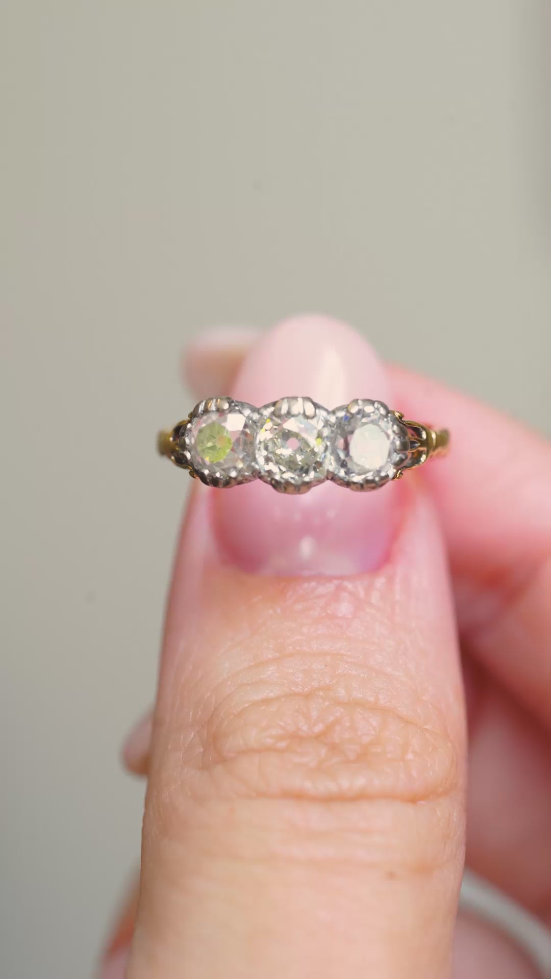 A video of an Antique three-stone diamond engagement ring held between the fingers and turned to show angles.