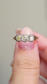 A video of an Antique three-stone diamond engagement ring held between the fingers and turned to show angles.