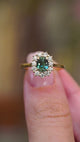 A video of an antique-inspired teal sapphire and diamond halo ring held between the fingers.