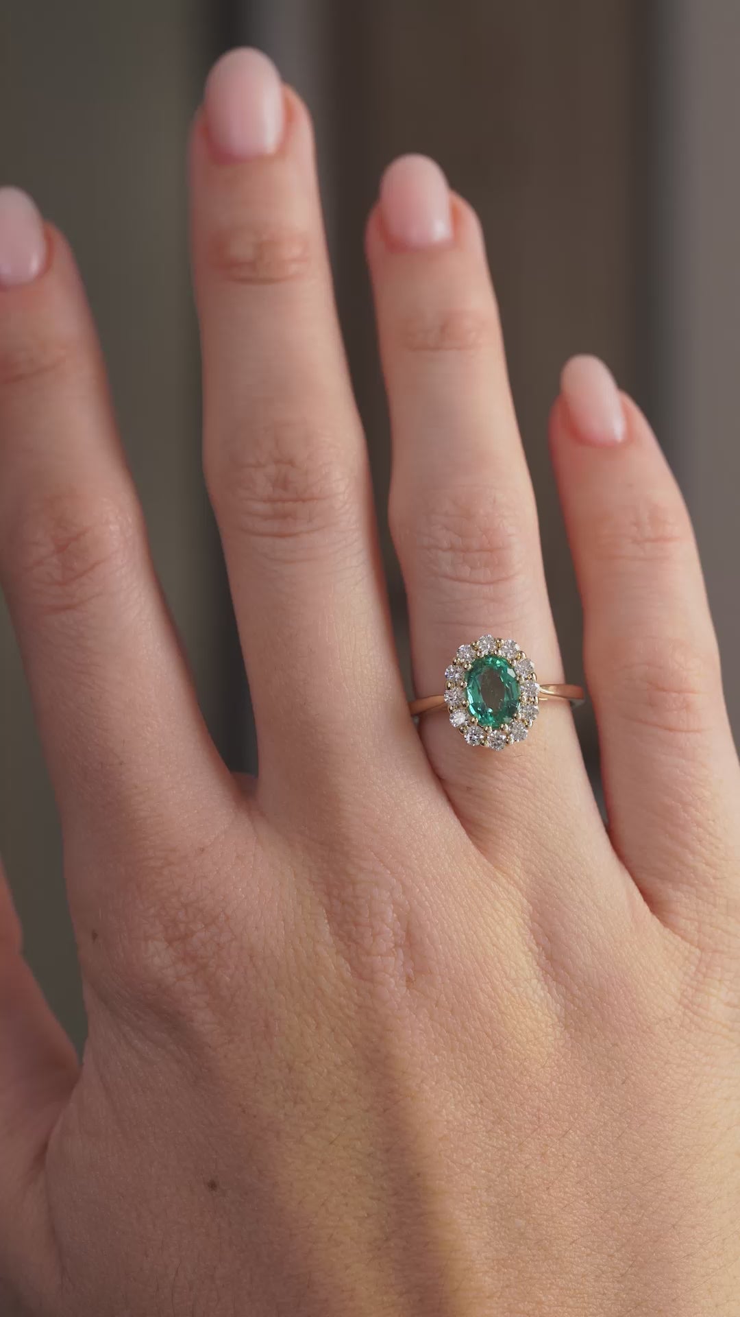 Handheld portrait of the oval emerald encircled by bright round diamonds in a refined gold setting.