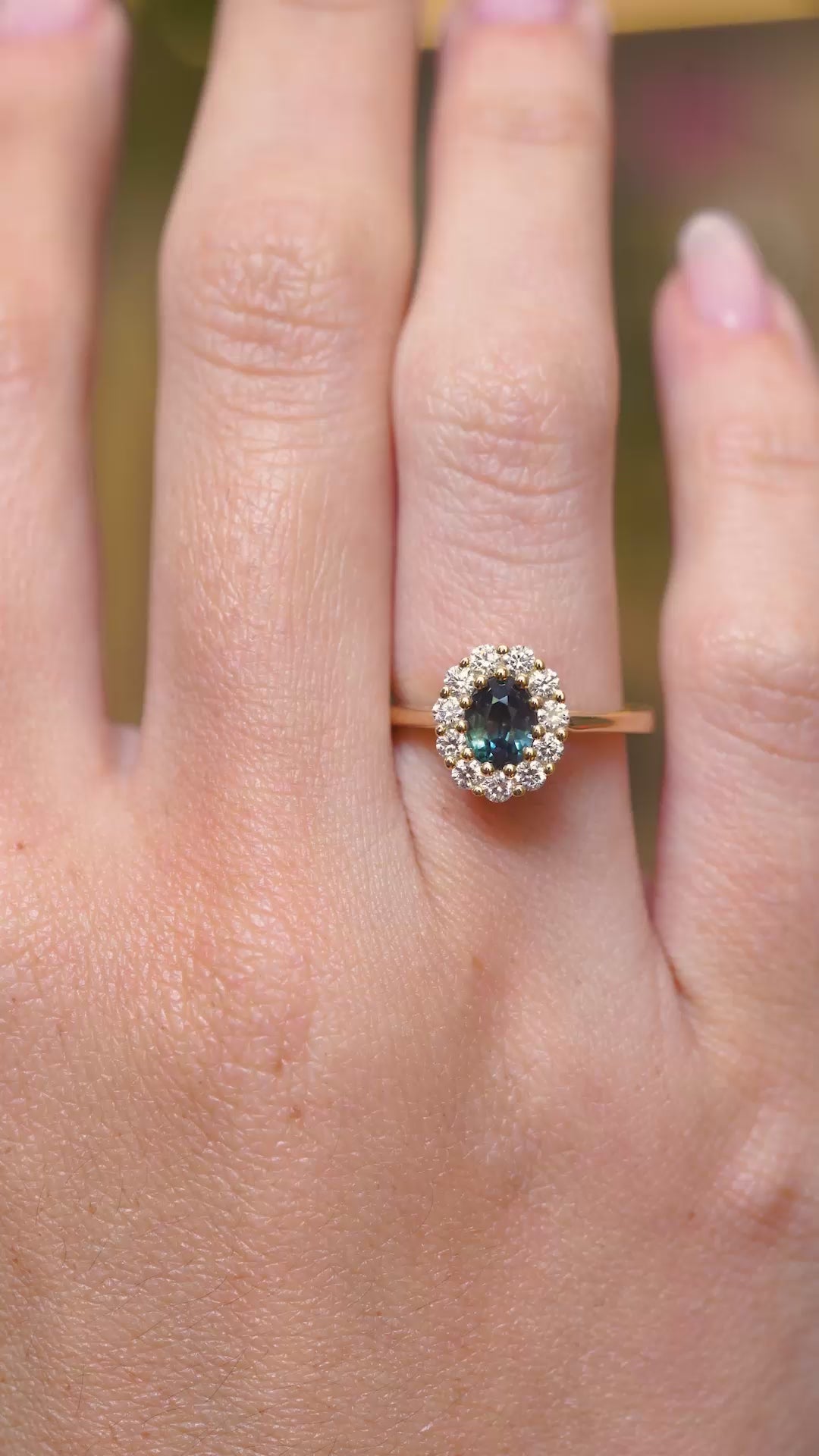 A video of a deep green sapphire and diamond cluster engagement ring in yellow gold displayed on the hand.