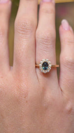 A video of a deep green sapphire and diamond cluster engagement ring in yellow gold displayed on the hand.