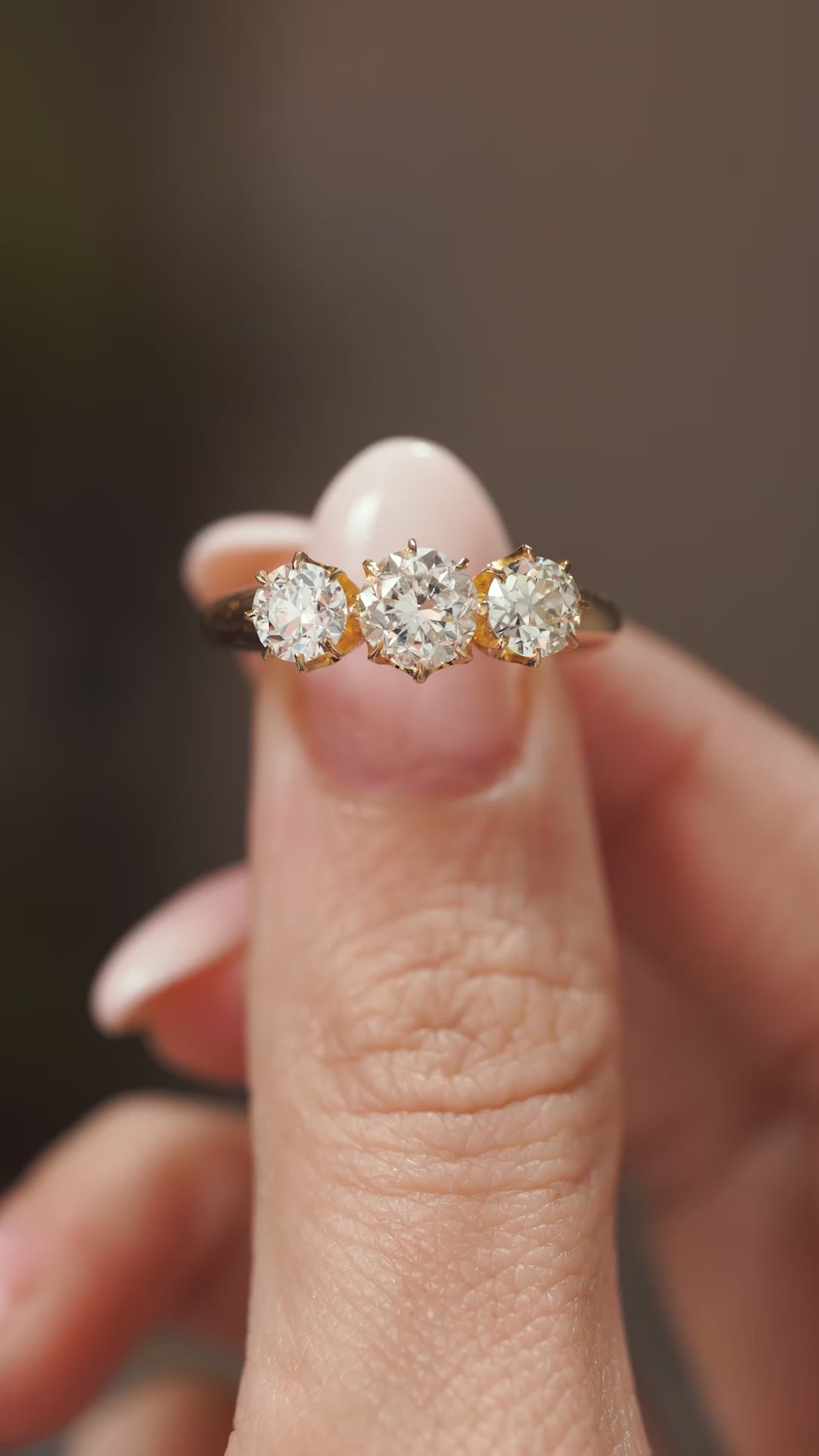 Video close-up of a vintage 1930s three-diamond engagement ring balanced on a fingertip, revealing the claw-set antique stones.