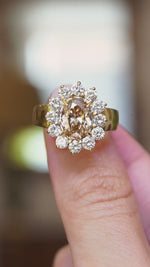 A close-up video of a vintage brown diamond engagement ring with a diamond halo cluster in yellow gold held between fingers.
