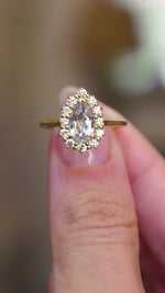 A video of a vintage-inspired pear-cut white sapphire and diamond cluster ring held between the fingers.