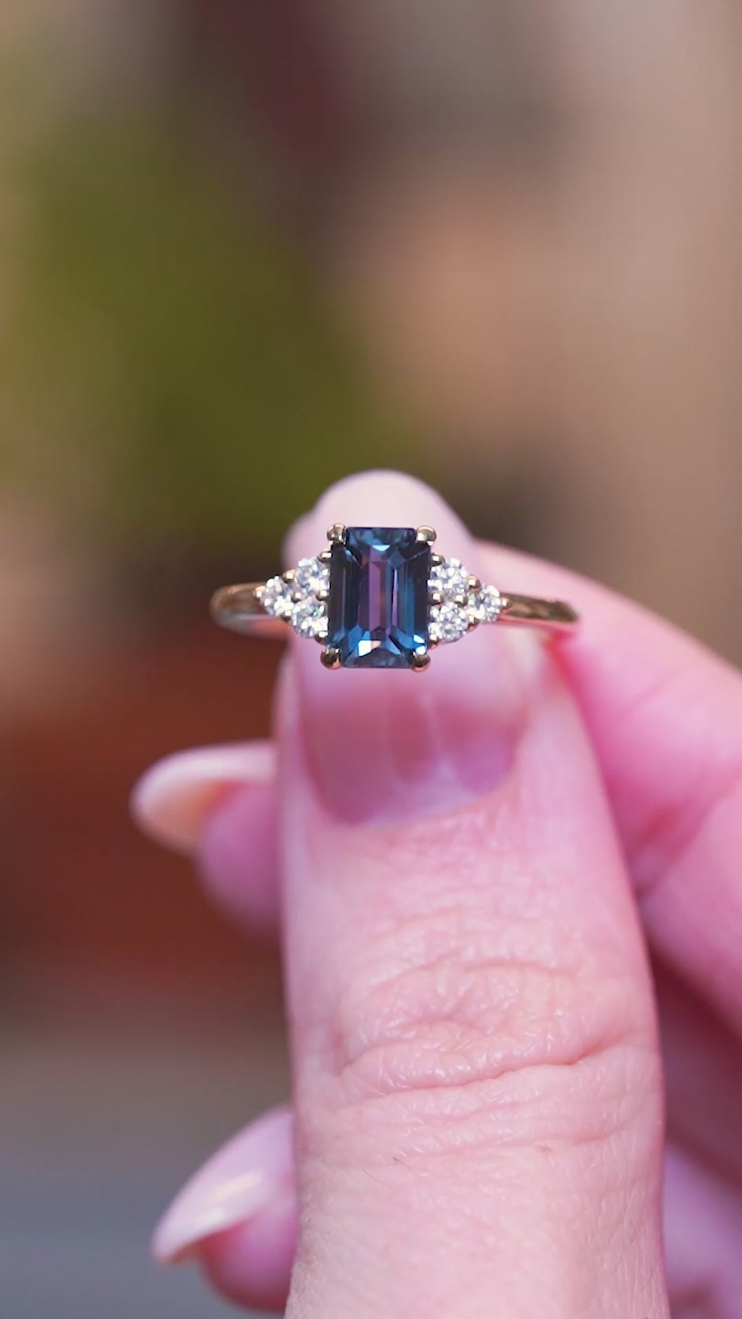 Teal sapphire and diamond cluster tre-foil engagement ring held between fingers with movements showing the ring details.