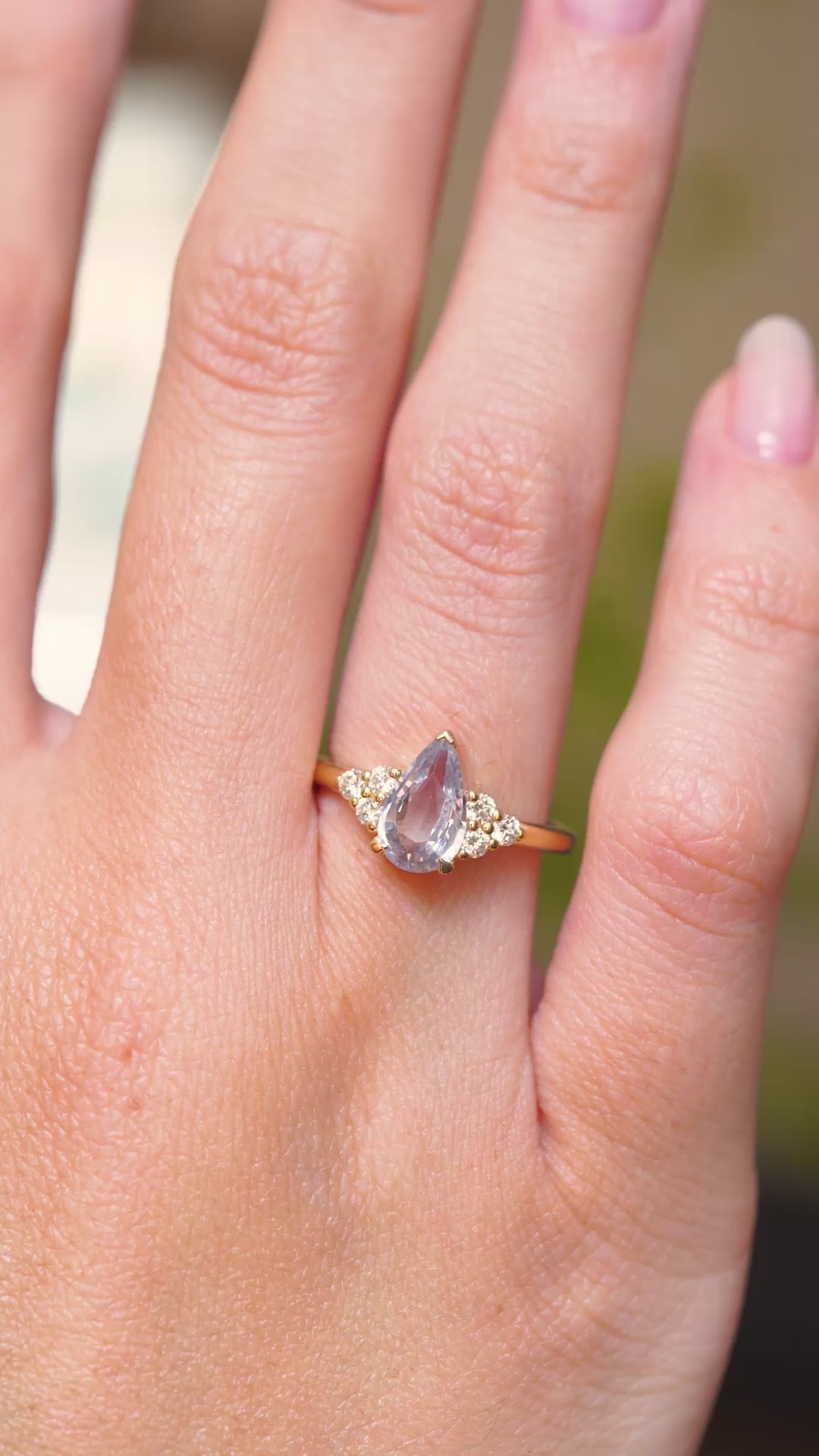 A video of a white pear-cut sapphire and diamond trefoil engagement ring in yellow gold displayed on the hand.