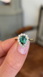 Antique-inspired pear-cut teal tourmaline and diamond cluster engagement ring featuring a pear-shaped teal tourmaline and diamond halo, held by hand to showcase the setting and craftsmanship.