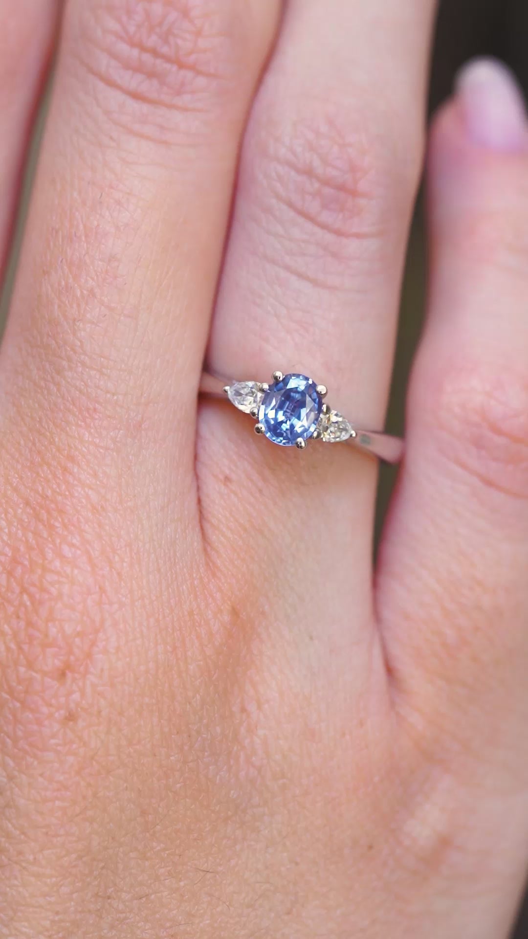 A video of a vintage-inspired light blue sapphire and diamond three-stone engagement ring worn on the finger.
