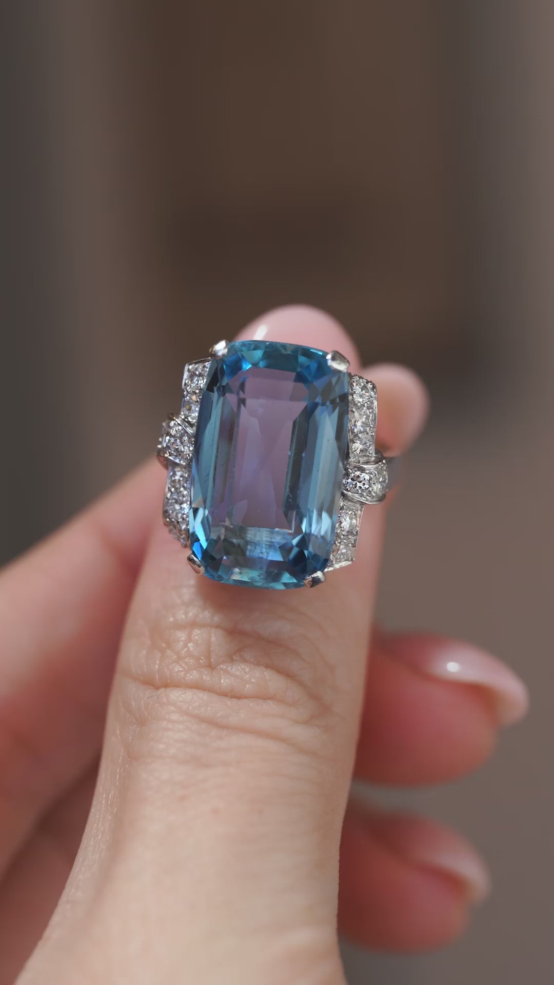 A close-up video of the aquamarine cocktail ring held between fingers, showcasing its vivid blue gemstone and intricate diamond shoulders.
