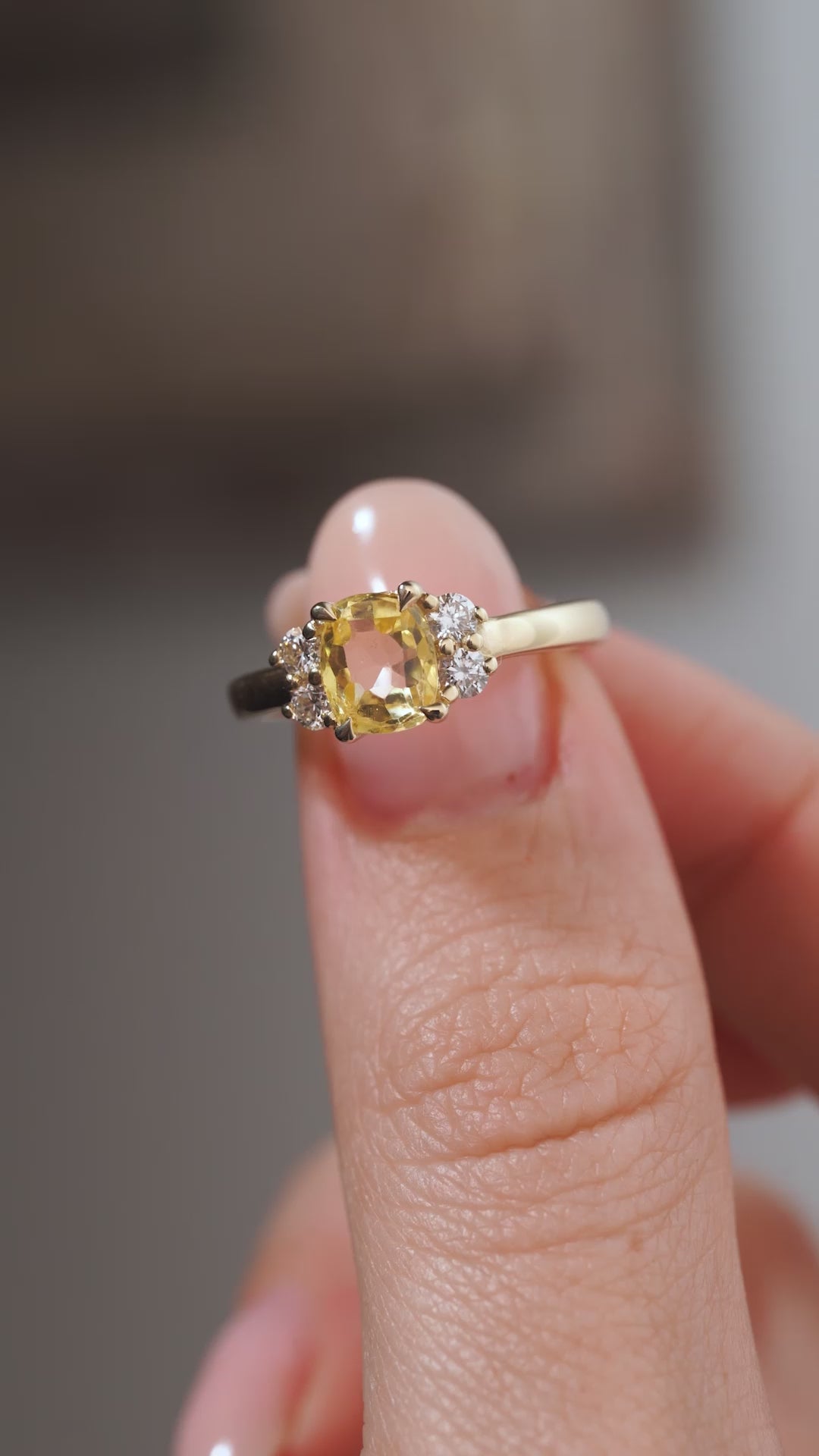 A close-up video of the vintage-inspired yellow sapphire and diamond ring held between fingers, displaying the cushion-cut gemstone's delicate facets and sparkling diamond clusters.