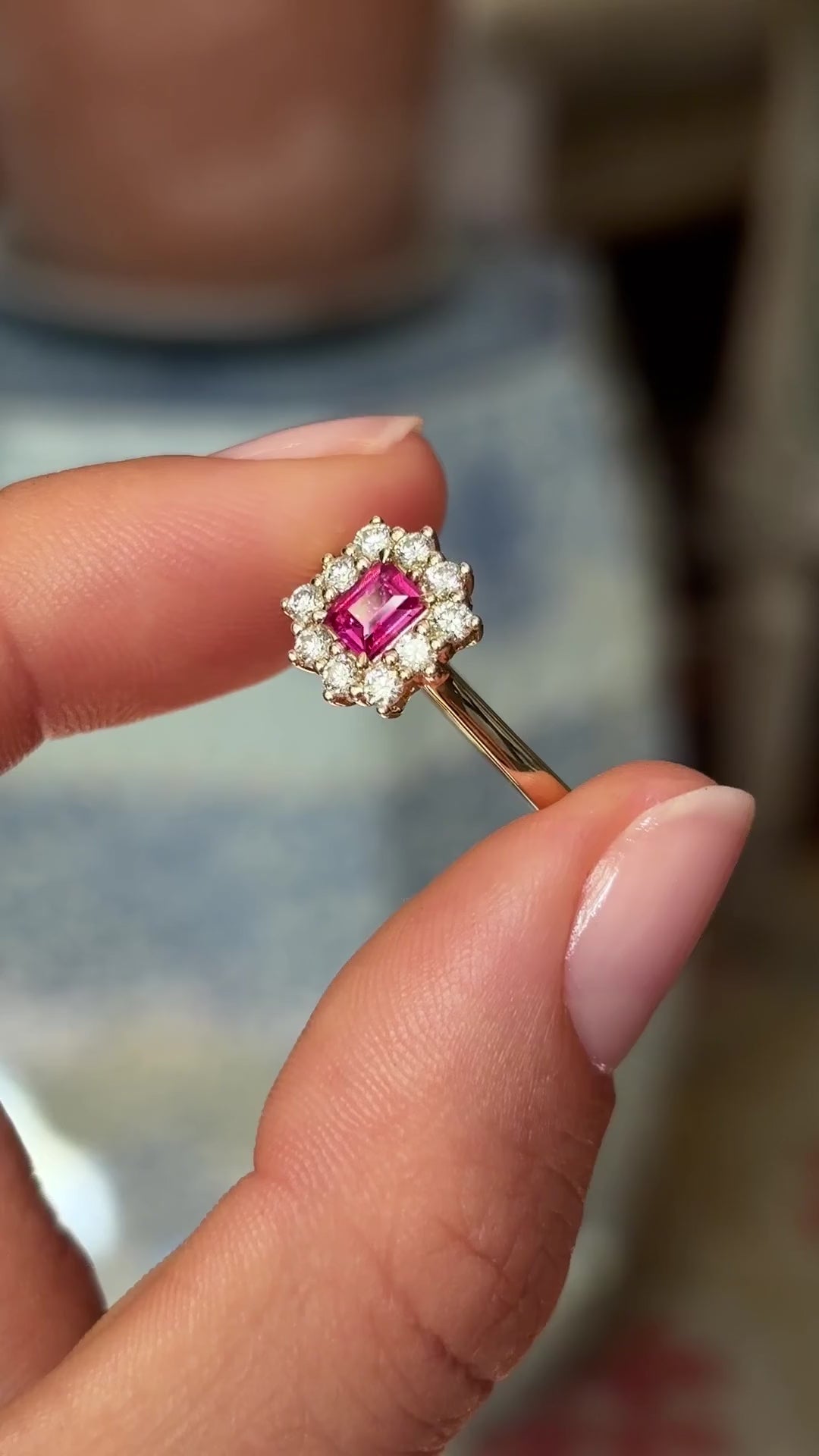 Rectangular step-cut ruby and diamond cluster gold engagement ring featuring a rectangular step-cut ruby encircled by diamonds, held by hand for detailed viewing.